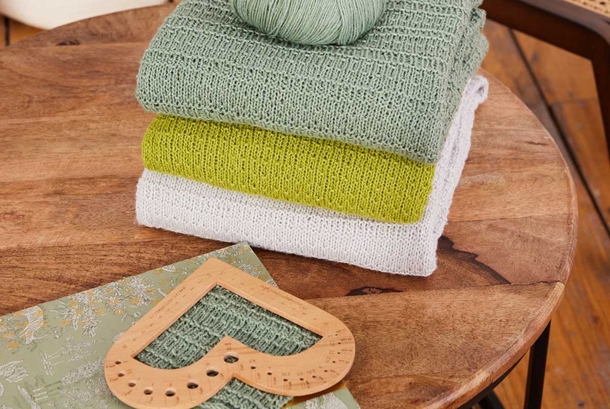 gestrickte Pullover gestapelt, davor liegend ein Nadelmesser aus Holz