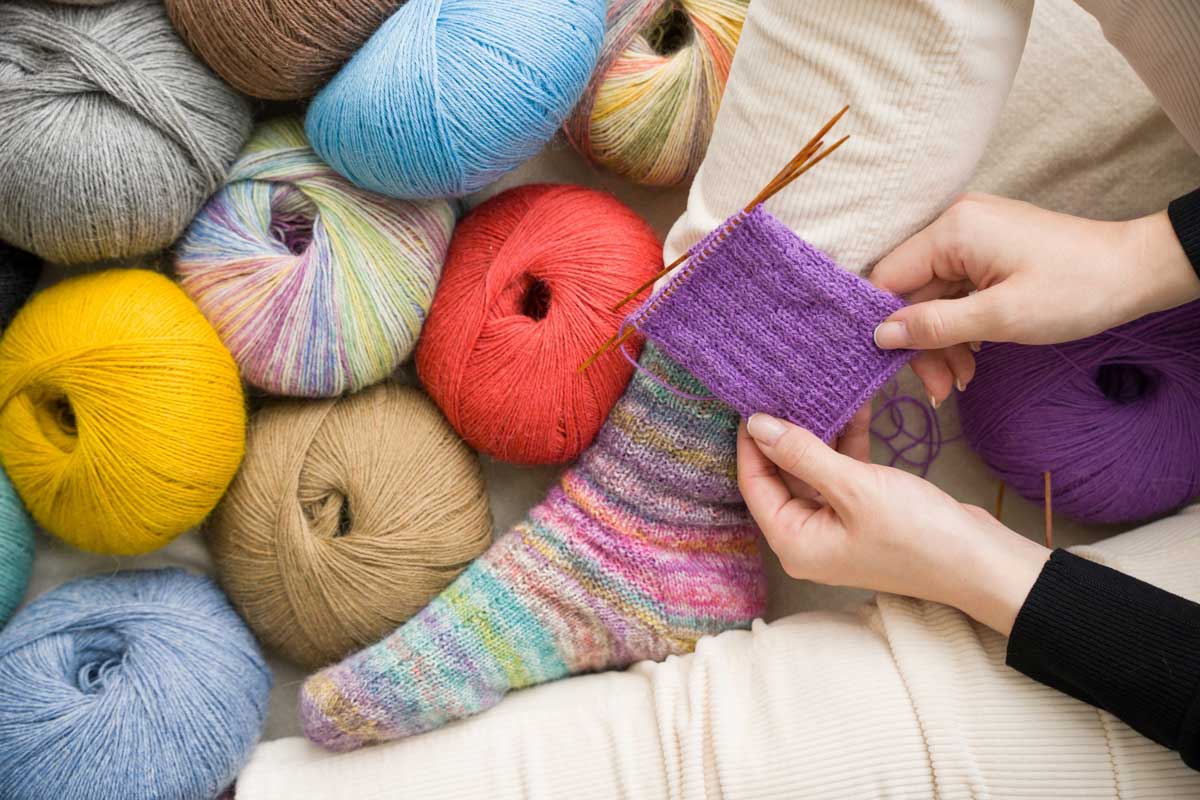 Wollknaeuel und gestrickte bunte Socke und einem angefangenem Bund auf dem Nadelspiel