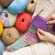 Wollknaeuel und gestrickte bunte Socke und einem angefangenem Bund auf dem Nadelspiel